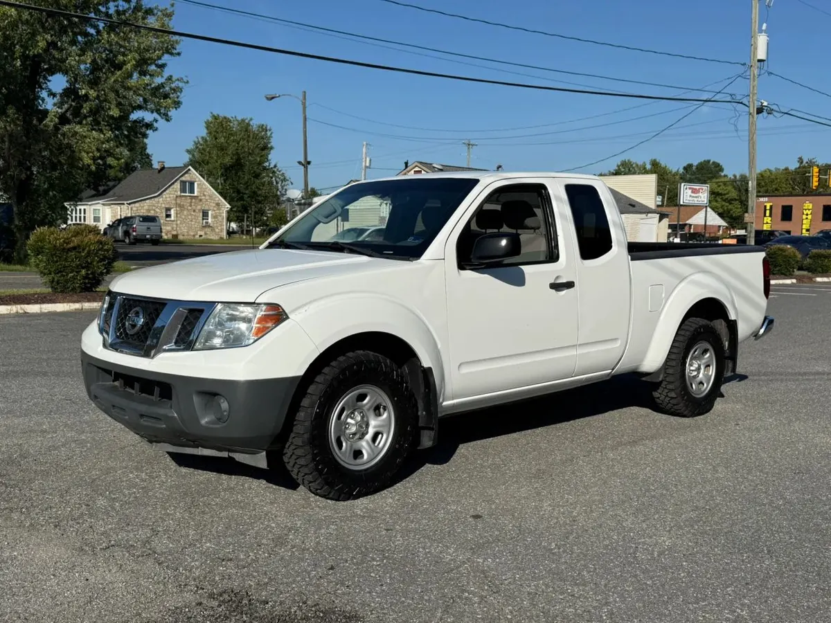 A white Nissan Frontier King Cab pickup truck parked on a paved lot, seen from the front driver's side