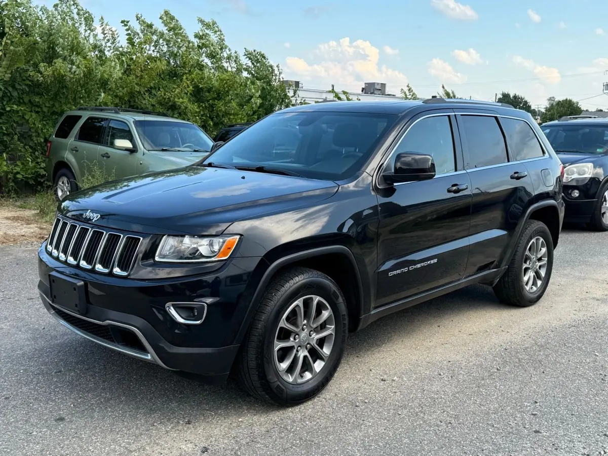 A black Jeep Grand Cherokee parked on a gravel lot, seen from the front driver's side