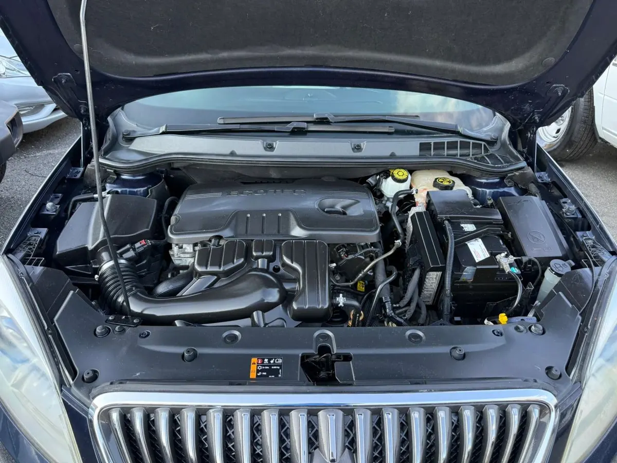 The engine bay of a Buick Verano with the hood raised, showing the engine cover, fluid reservoirs and battery