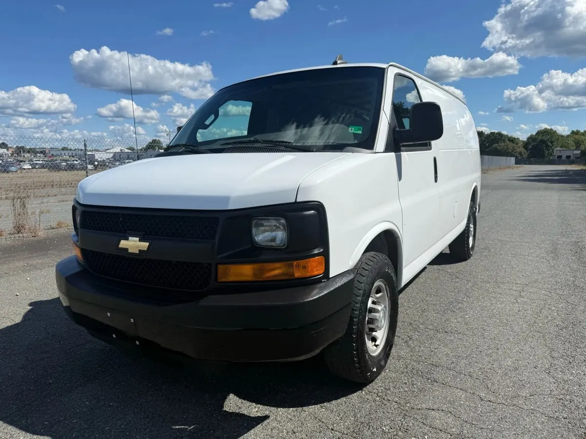 A white Chevrolet Express cargo van parked on open pavement under a blue sky, seen from the front