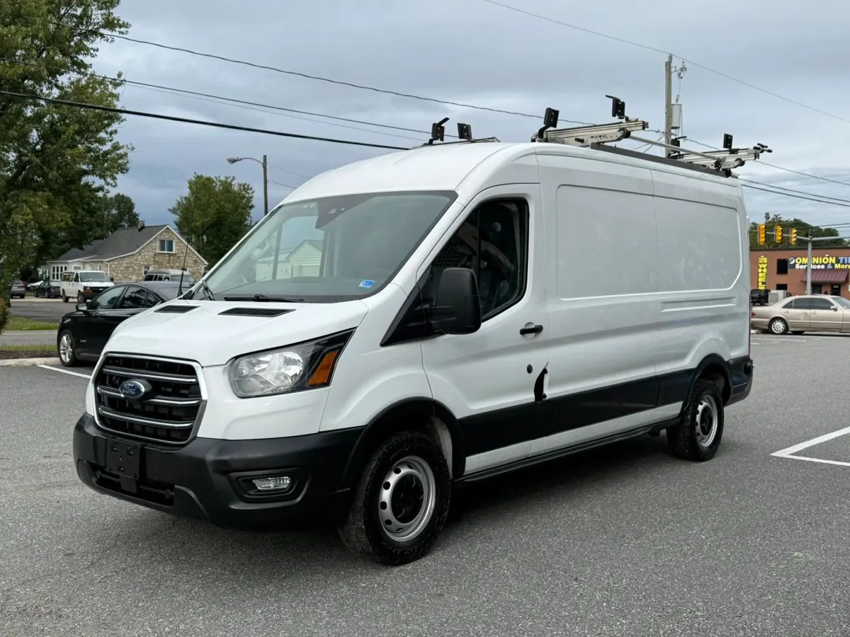A white Ford Transit medium-roof cargo van with roof ladder racks parked on the Mix Cars lot
