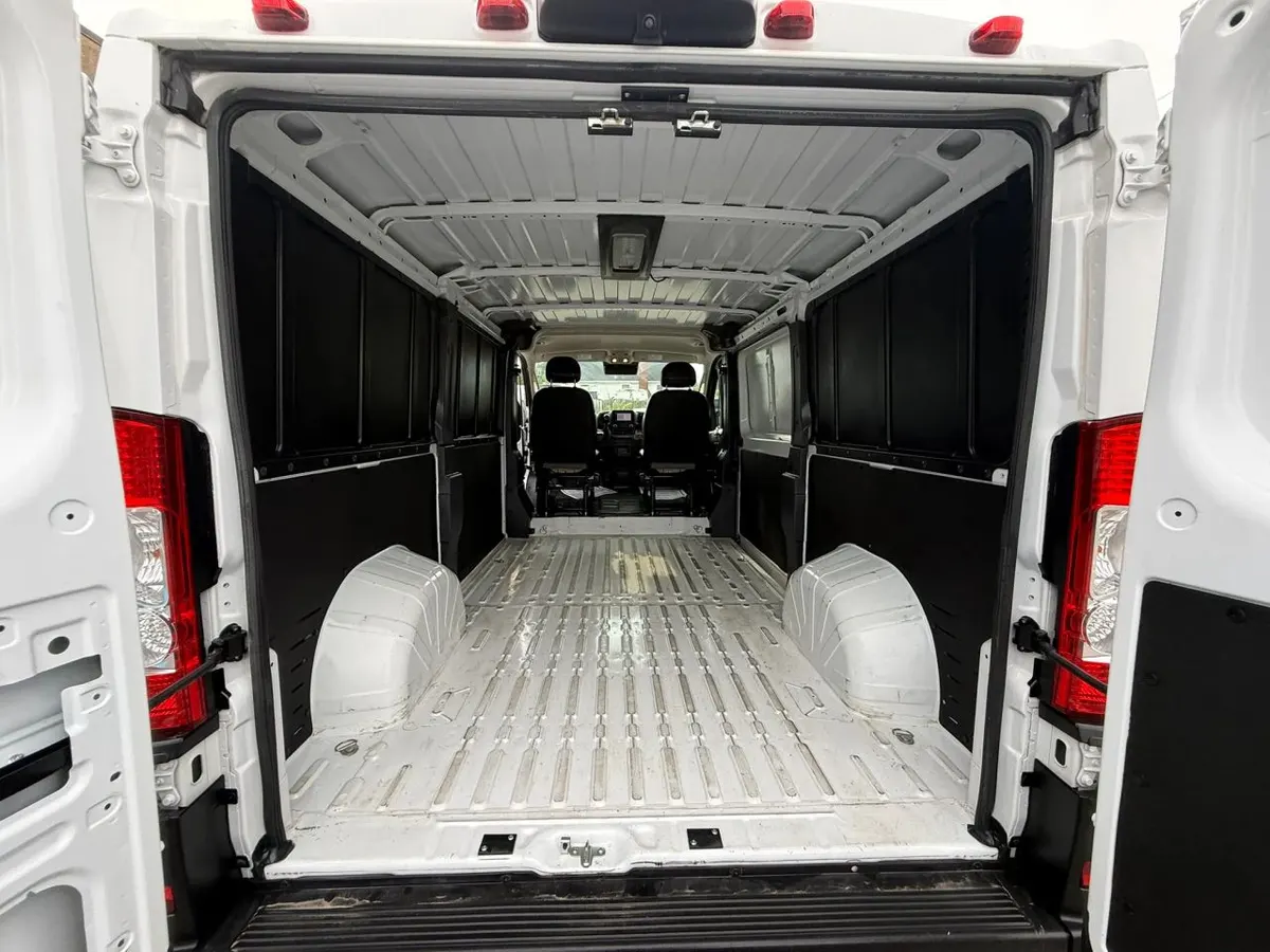 The empty cargo area of a RAM ProMaster low-roof van seen through its open rear doors, with the wheel wells and cab seats visible
