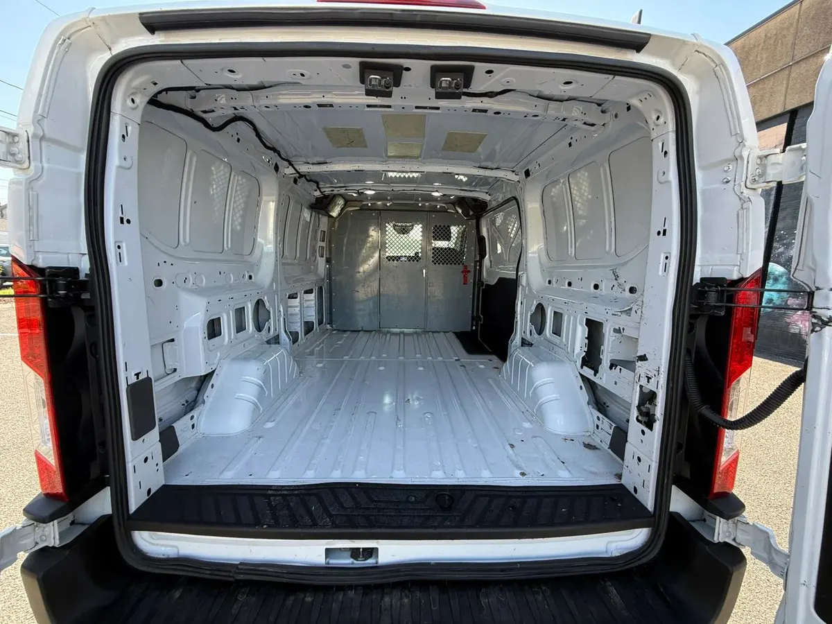 The empty cargo area of a Ford Transit low-roof van seen through its open rear doors, with a partition behind the seats